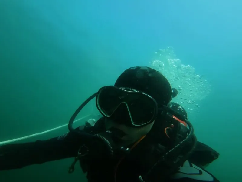 Scuba diver underwater with bubbles rising in a greenish blue sea.
