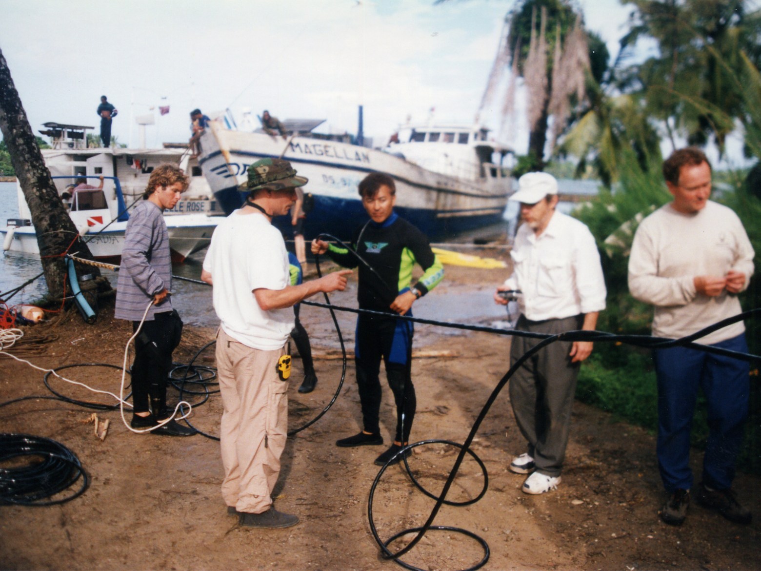 People on a riverbank handling cables with boats in the background.