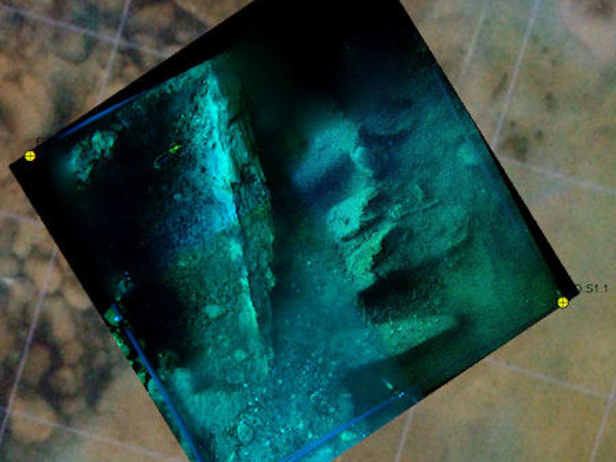 Underwater image of a sunken structure with rocks and debris on the sea floor.