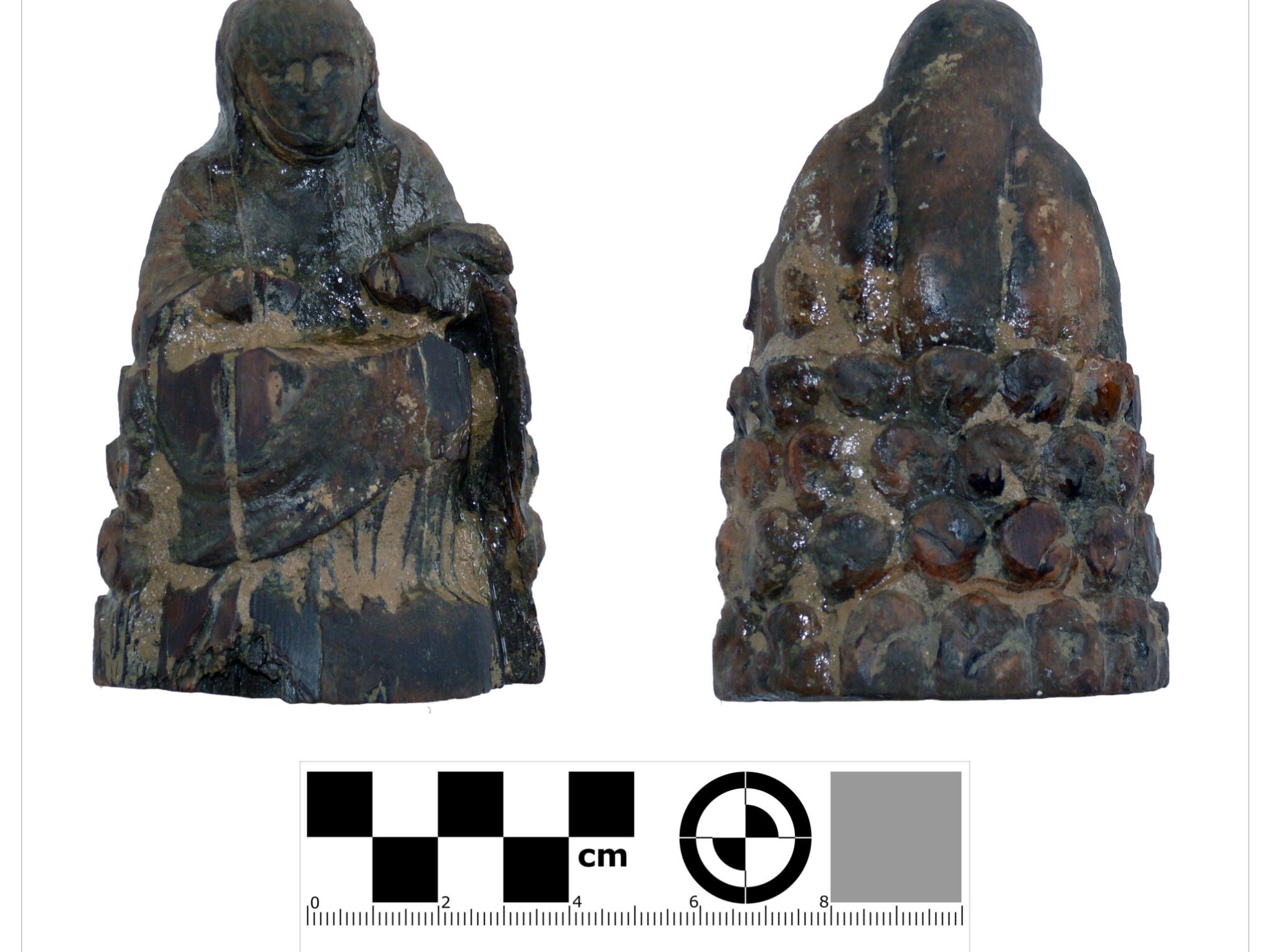 Two small, dark figurines with one front and one back view, next to a measurement scale in centimeters.